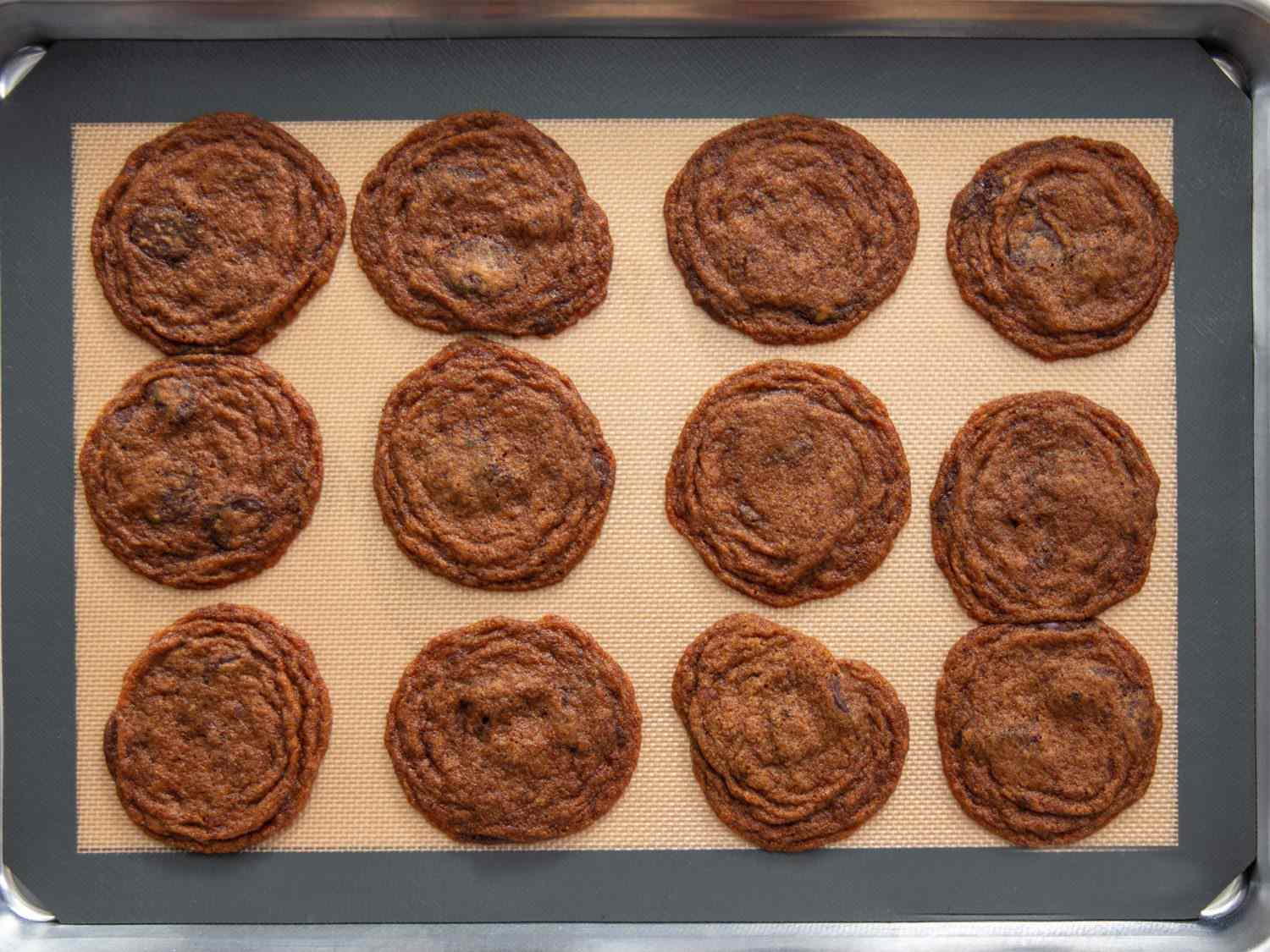 Dark brown cookies on a baking sheet lined with a silicone mat, showing excess spread and rippling of cookies baked on silicone.