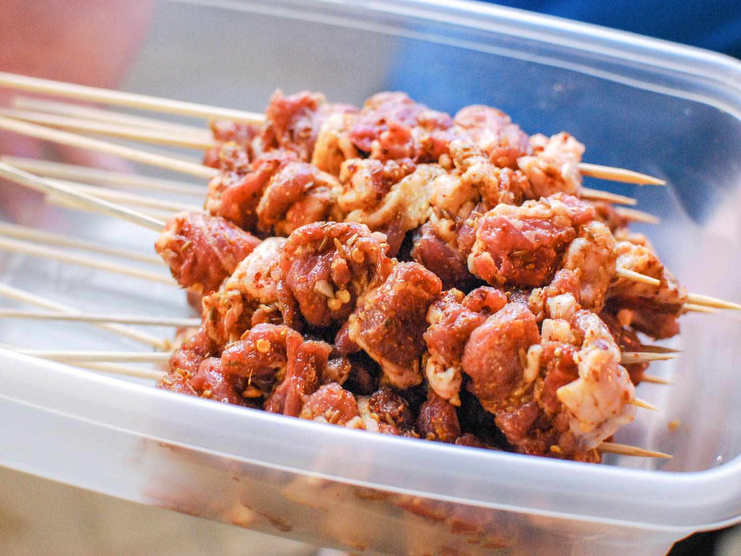 Several seasoned, uncooked lamb skewers resting in a plastic container. 