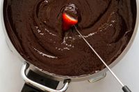 A fondue fork dragging a strawberry through chocolate fondue.