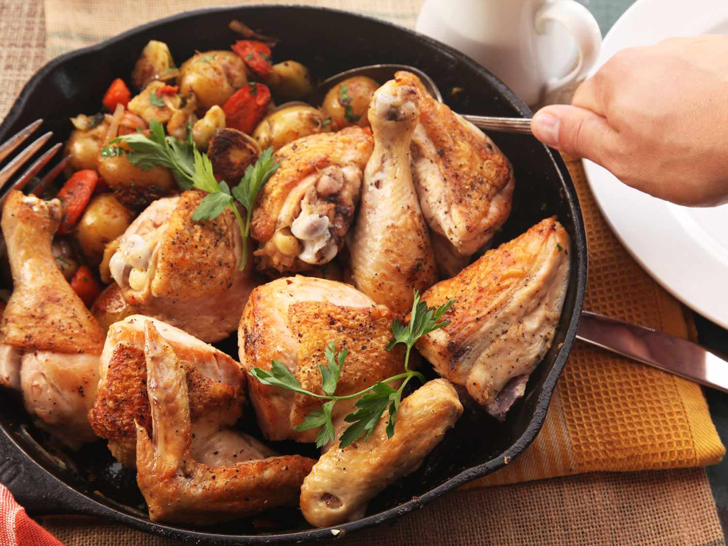Placing a spoon into a skillet filled with roasted chicken and vegetables
