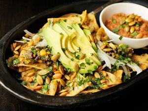 Chilaquiles with pepitas, charred corn, and black beans are served in a black earthenware platter.