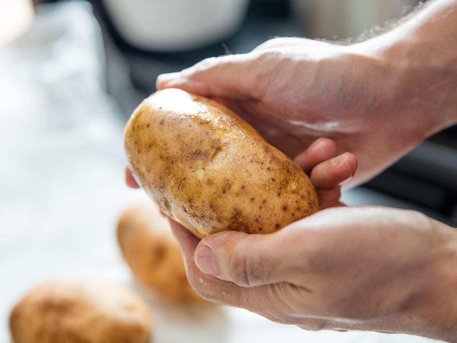 Two hands washing potato in sink.