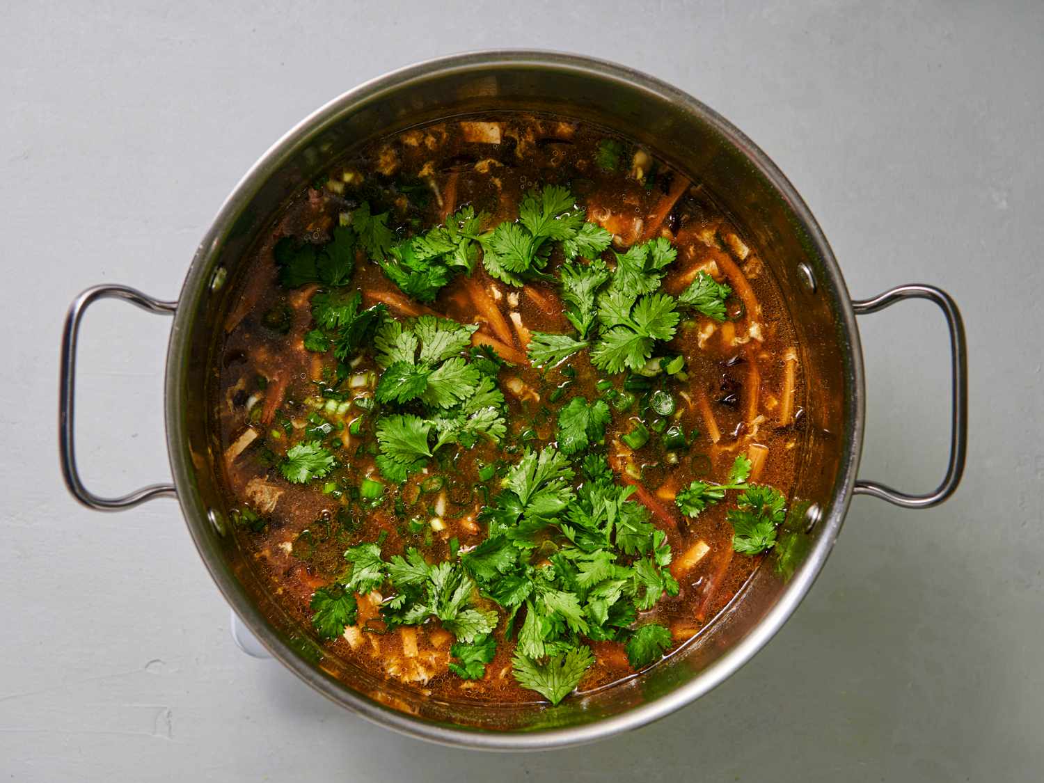 The contents of the pot now with white pepper and vinegar stirred int, sesame oil drizzled in, and scallions and cilantro sprinkled on the surface.