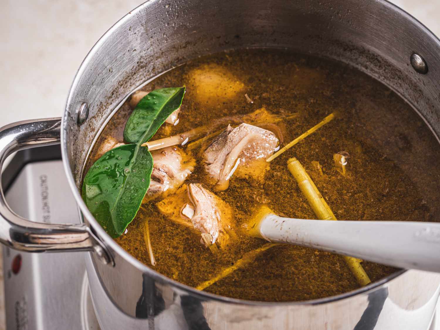 Lemongrass and lime leaves added to a stockpot full of broth.
