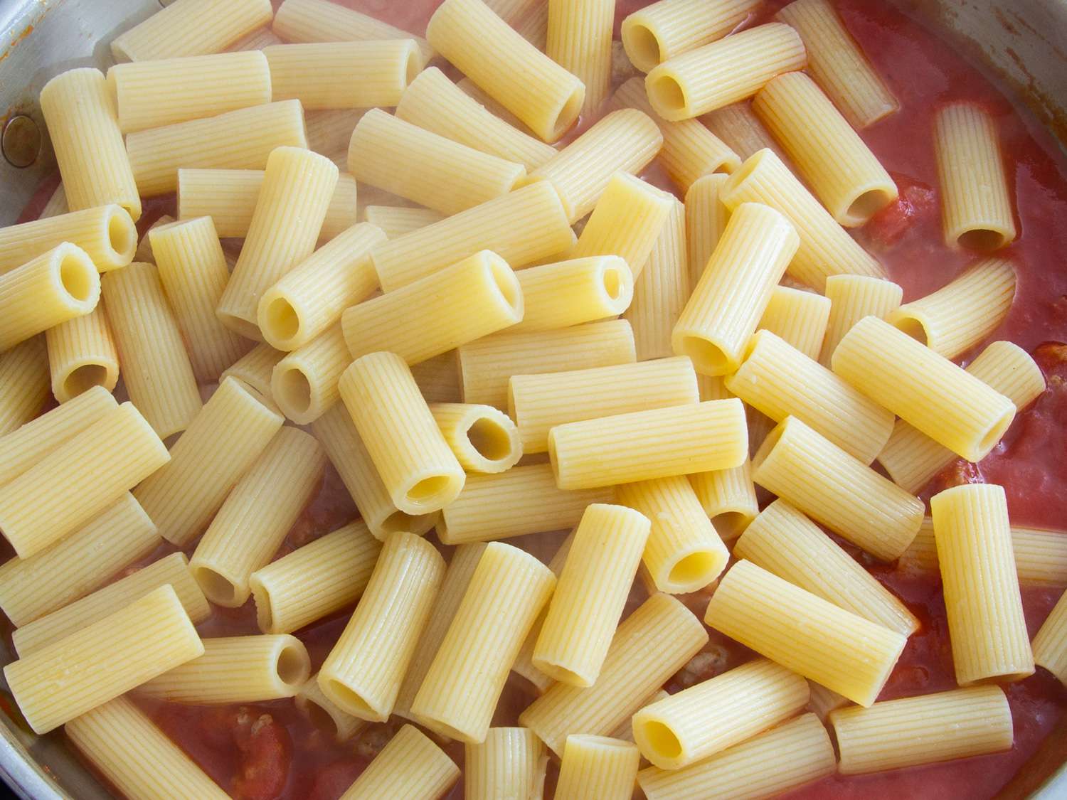 Cooked pasta noodles being added to the sausage and tomato mixture.