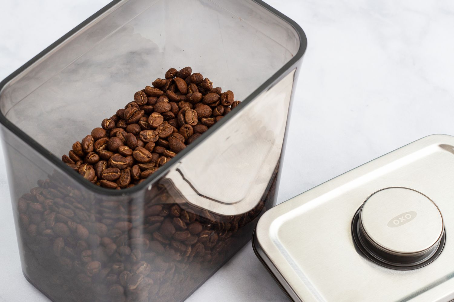 The OXO POP Coffee Container filled with coffee beans with the lid off sitting on a marbled surface