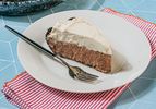 A slice of pie with whipped topping served on a plate with a fork on a striped napkin