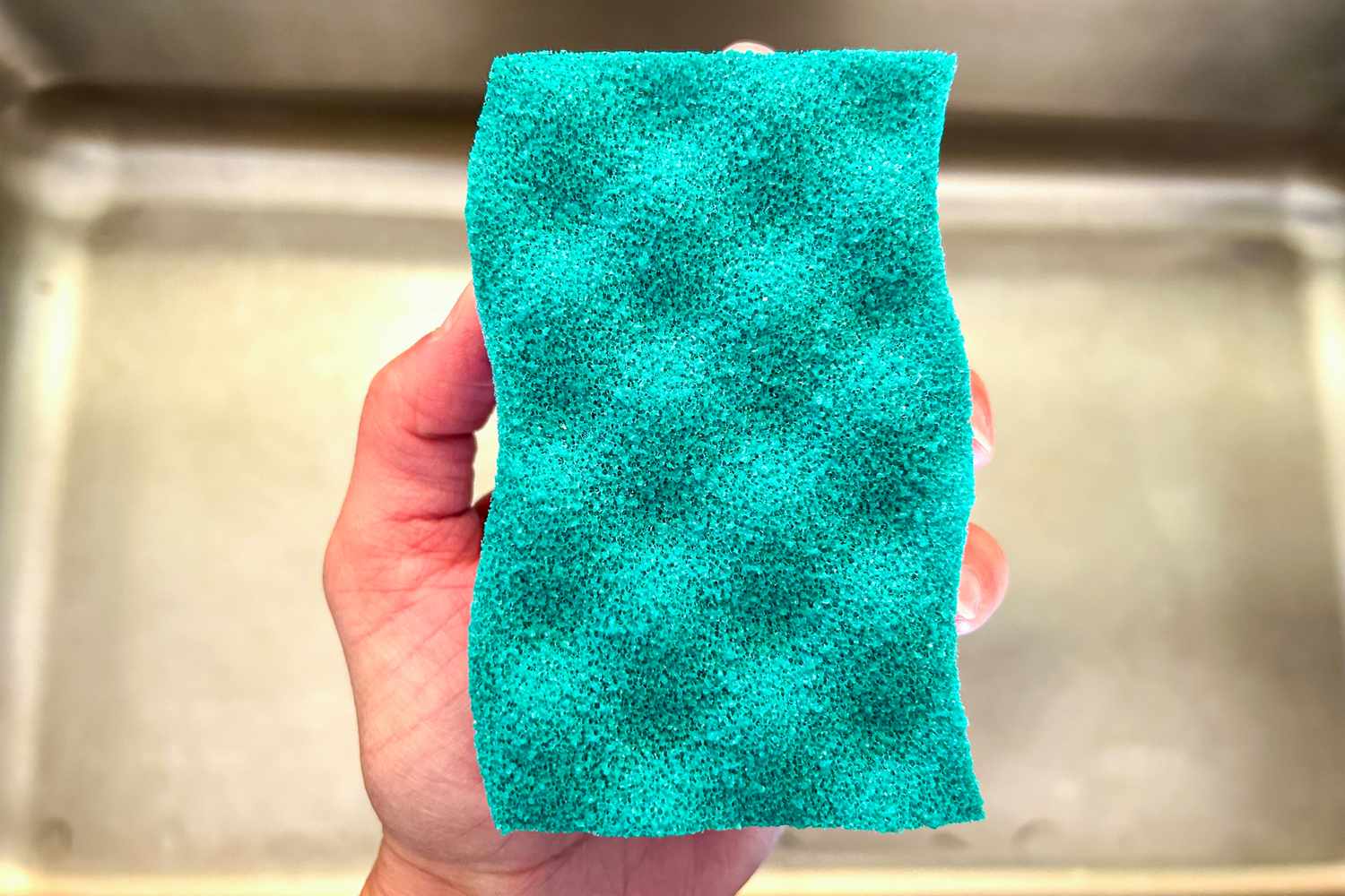 An O-Cedar Scrunge being held over a stainless steel sink