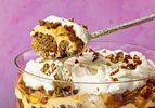 Banana bread trifle with whipped cream and pecans in a glass bowl spoon scooping a portion