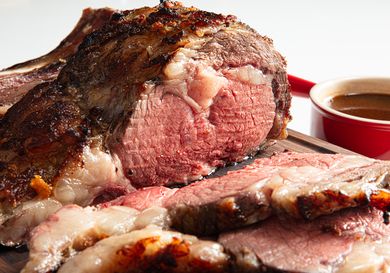 Sliced prime rib roast on a wooden board red dish in the background