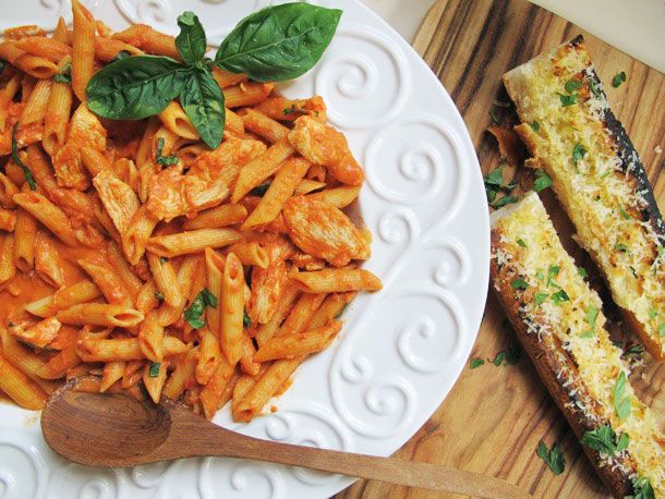 Overhead of a serving dish of chicken and penne in vodka cream sauce. Two pieces of cheesy garlic bread lie to one side.