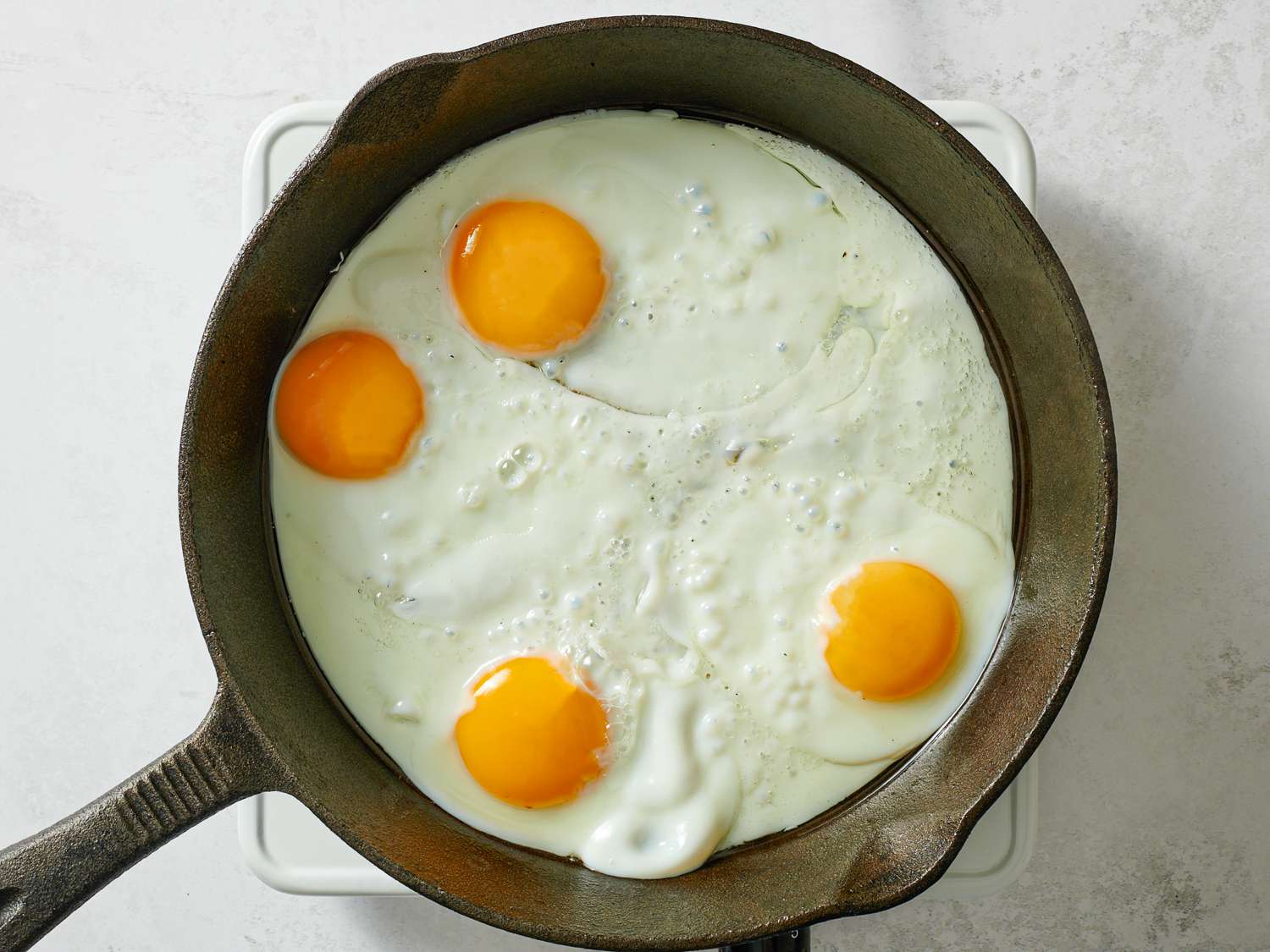 Four eggs being cooked in a cast iron skillet. The whites are set, while the egg yolks are intact and still runny.