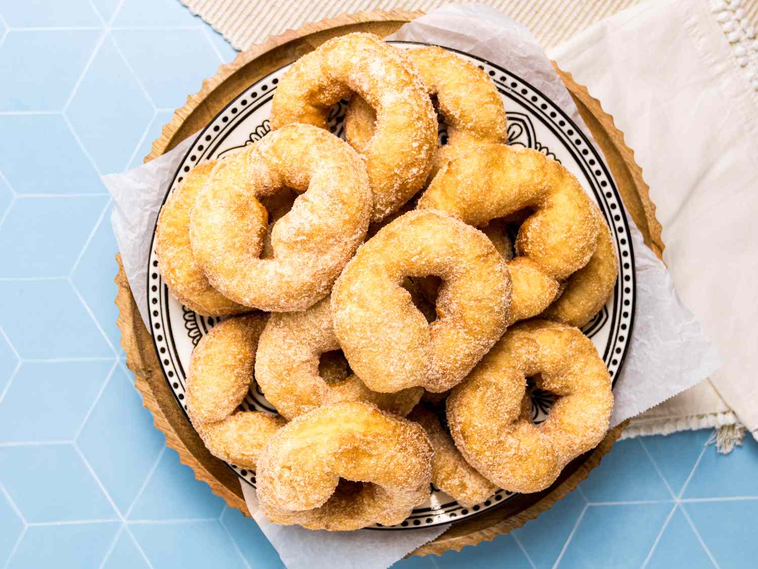 Plate of sfenj donuts arranged on a patterned dish with parchment paper