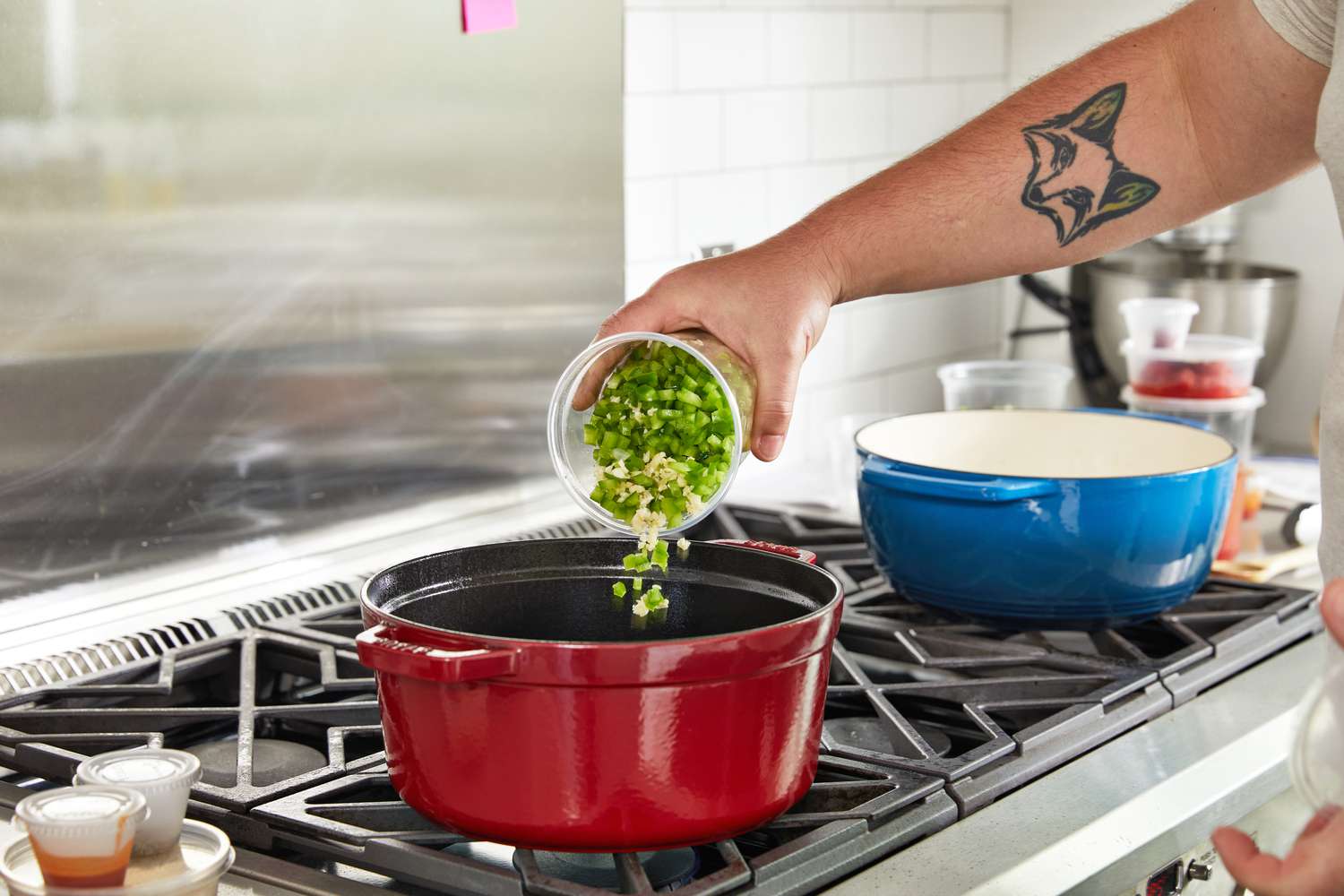 A hand adding finely chopped peppers and garlic to a dutch oven on the stovetop