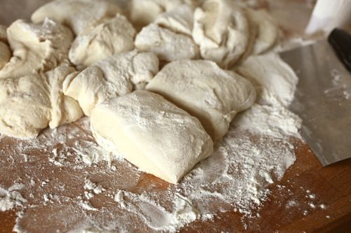 Flatbread dough on a floured work surface being portioned with a bench scraper.