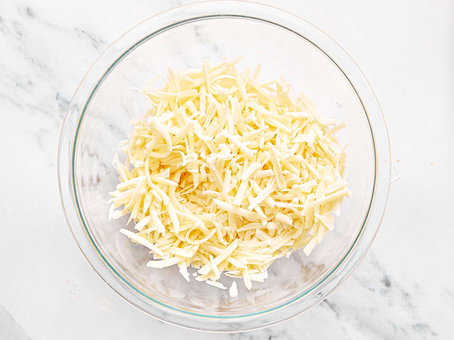 Shredded cheese in a glass bowl on a marble countertop