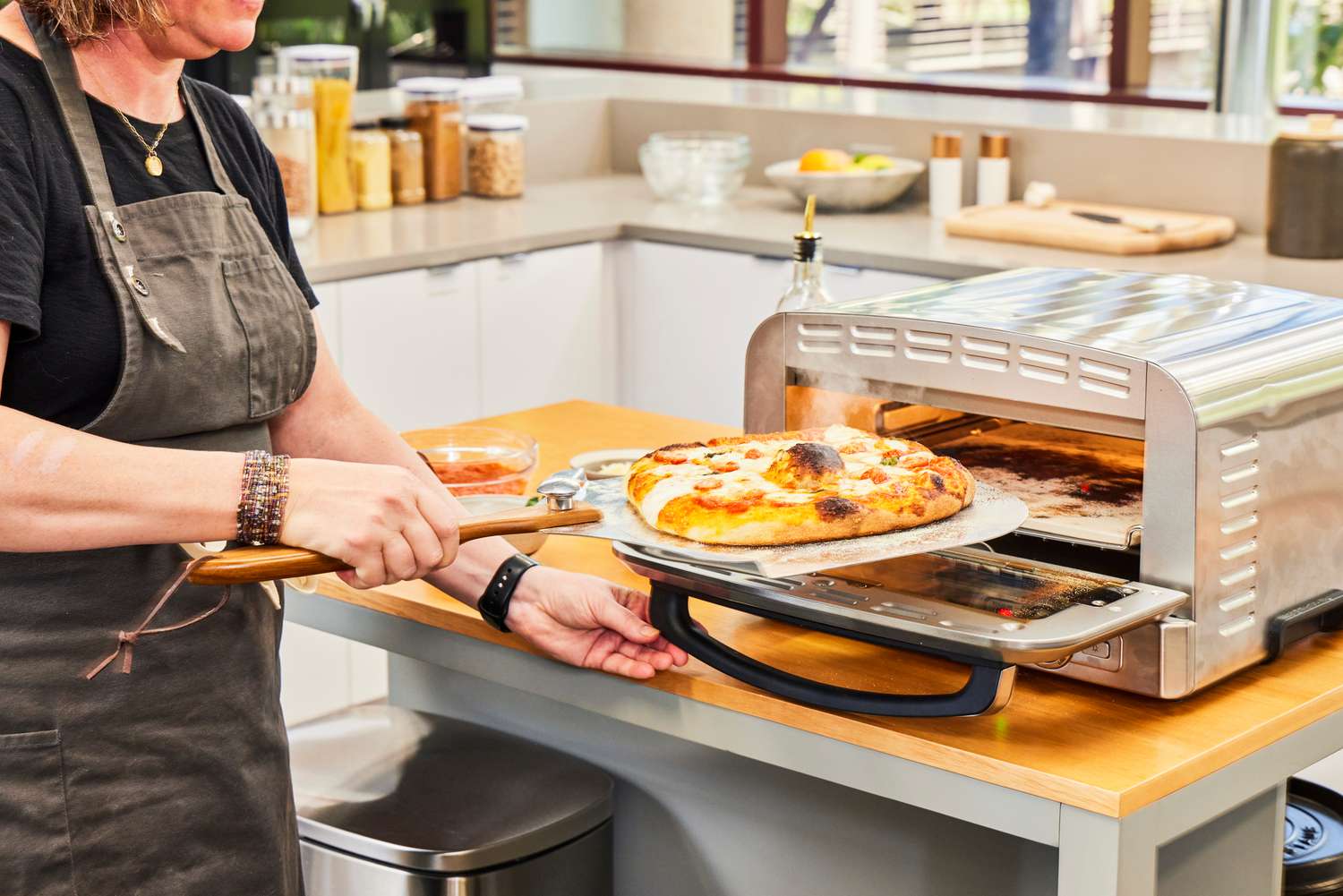 A person removes a pizza from the Cuisinart CPZ-120 Stainless Steel Indoor Pizza Oven