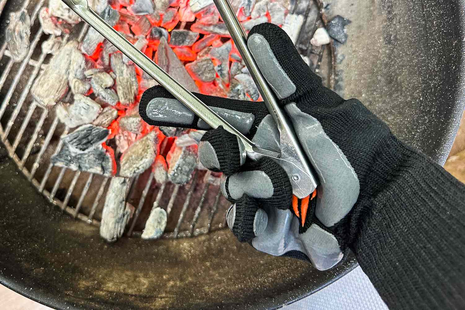A person holds tongs over hot coals while wearing the Blackstone Griddle Gloves