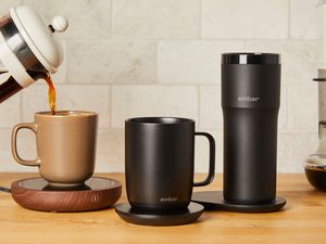 French press coffee is poured into a coffee mug on a warming pad, surrounded by two temperature control mugs