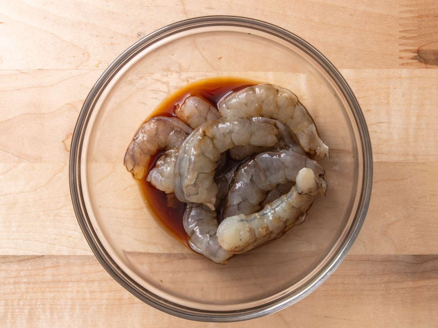 Shrimp marinating in sauce in a glass bowl