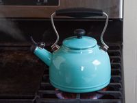 a blue kettle with steam coming out of the spout on a stove