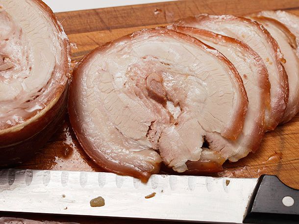 Chashu pork being thinly sliced on a cutting board with a large slicing knife.