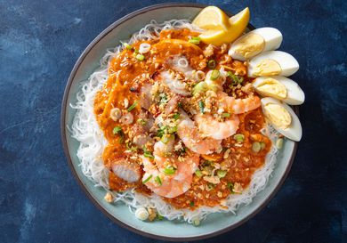 Overhead view of pancit palabok, served on an earthenware platter and garnished with lemon wedges and a quartered hard-boiled egg.