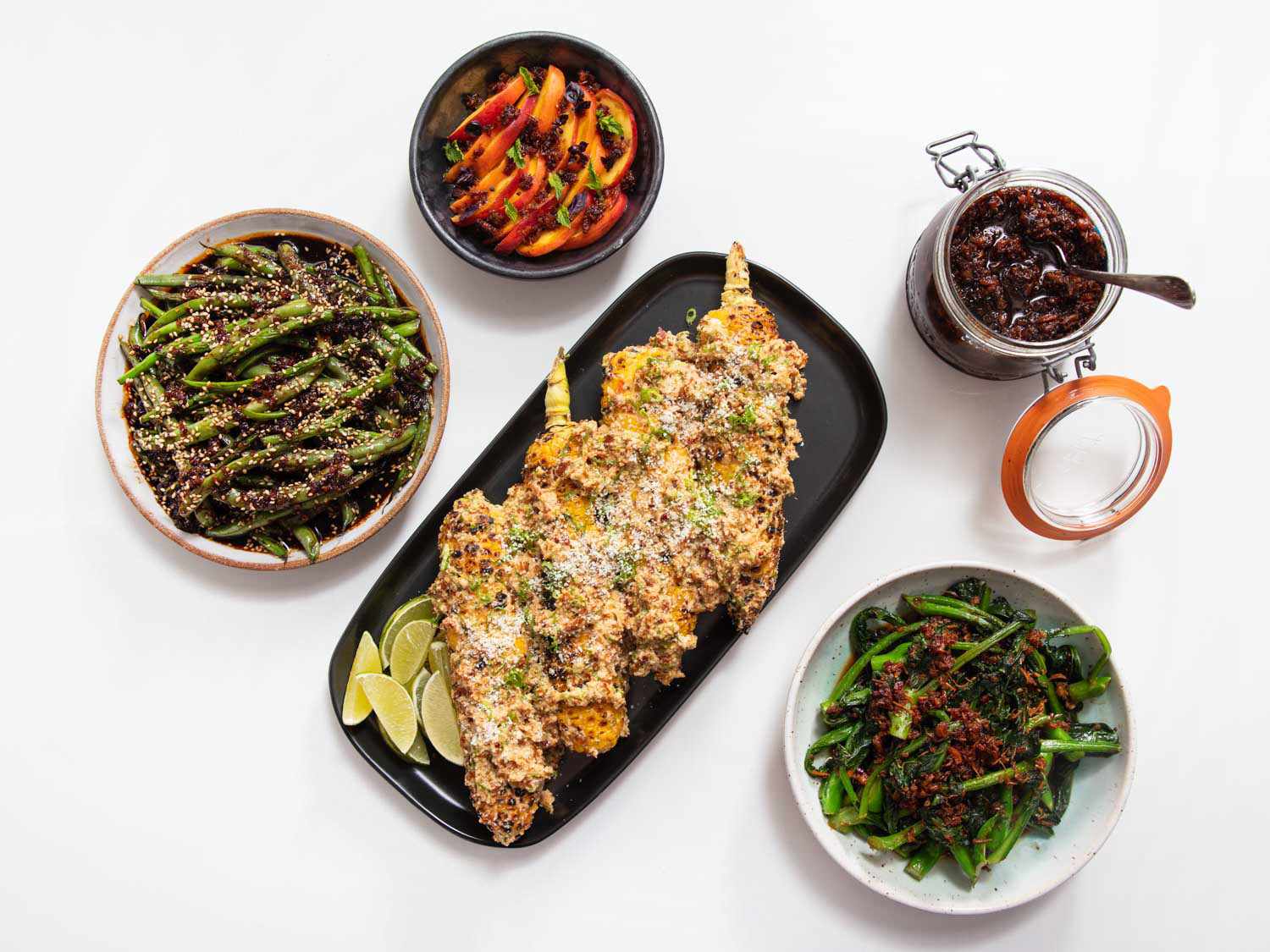Overhead of a spread of dishes using XO sauce, including charred Chinese broccoli, green beans, sliced peaches, and XOtes.