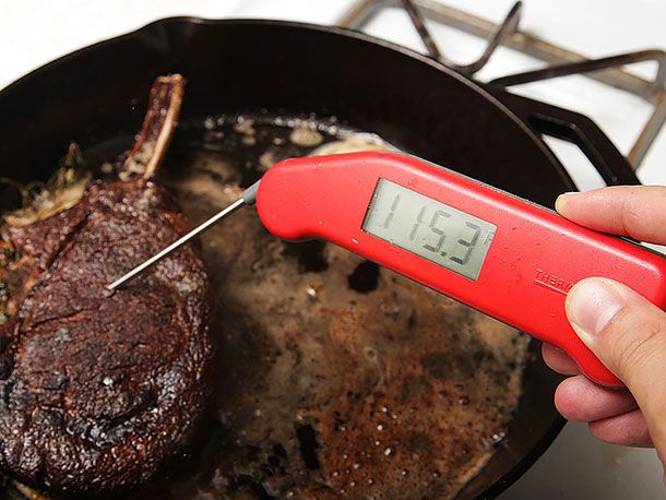Instant-read thermometer inserted into browned steak registers 115.3°F.