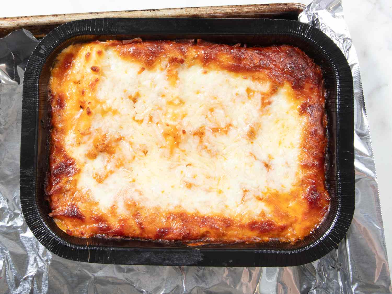 Baked frozen lasagna in a black tray on foil ready to be served