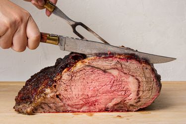 A cooked prime rib roast being carved with a knife and fork on a cutting board