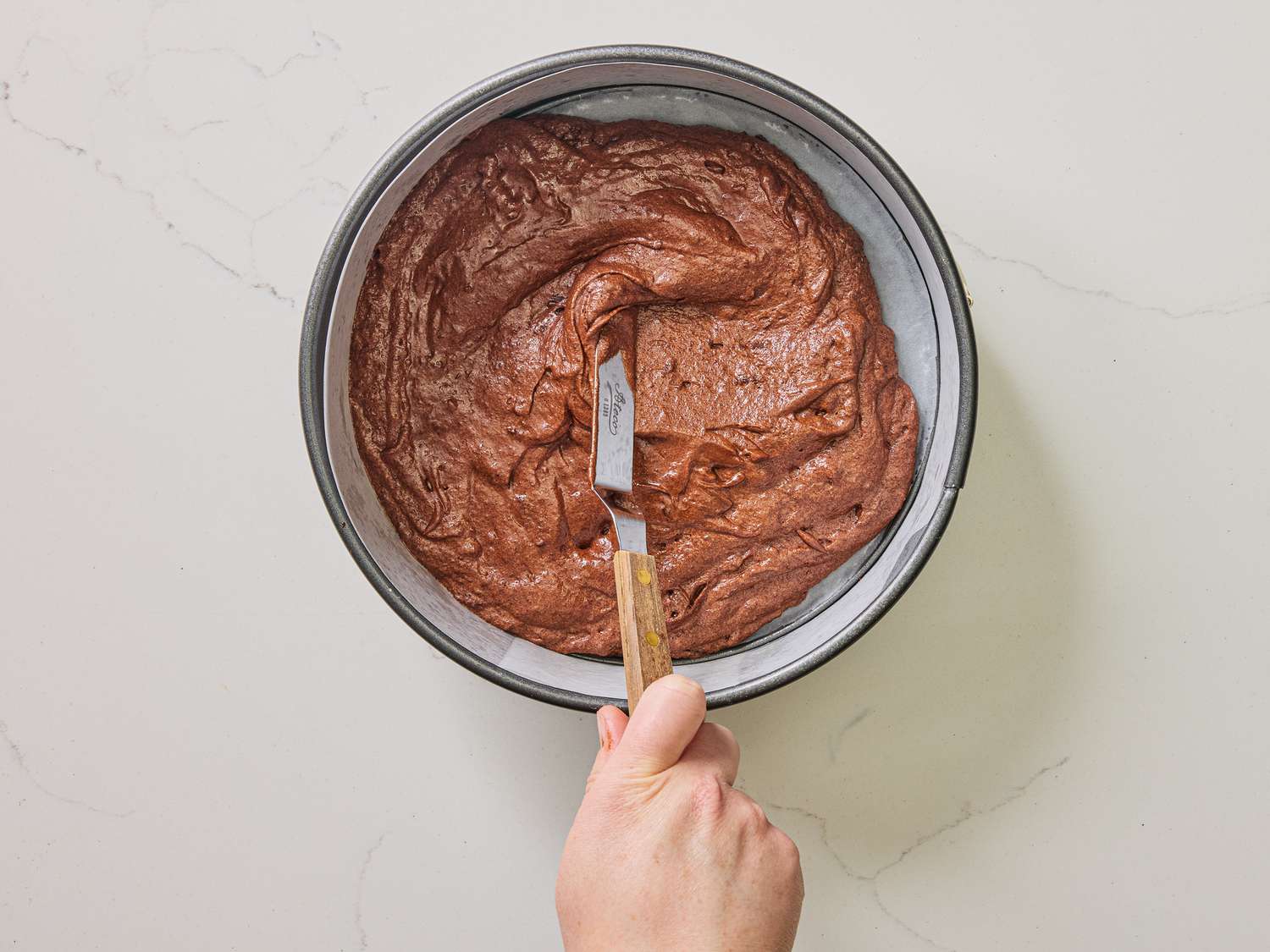 Using an offset spatula to spread the cake mix into round cake pan 