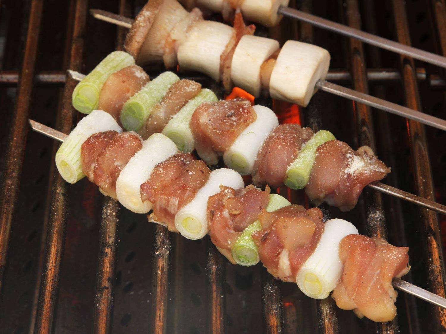 Raw chicken thigh yakitori and scallion on a grill. 
