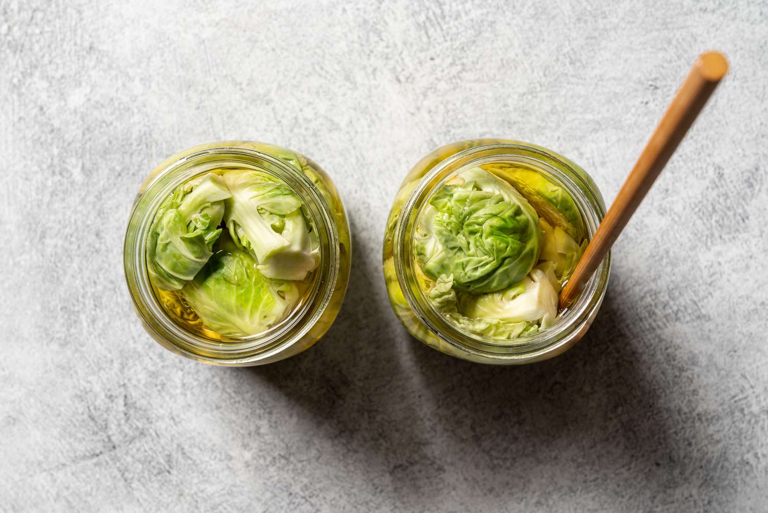A top-down view of the two jars of Brussles sprouts. The right jar holds a chopstick, which is used to help remove bubbles of air from around the sprouts.