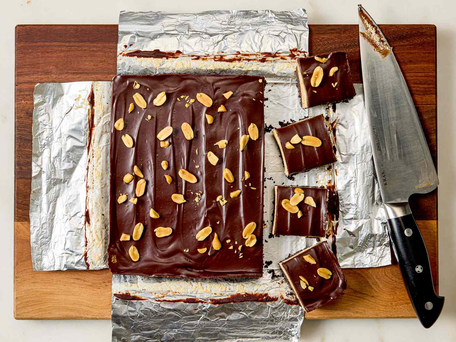 Chocolate peanut butter dessert on foil partially sliced into square servings with a knife nearby for serving