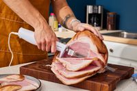 a person holding the hamilton beach electric knife and cutting slices of ham