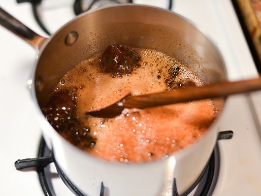 Reducing ham glaze down until it is thick and syrupy in a saucepan, stirring with a wooden spoon.