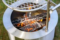 Close-up of a metal fire pit with burning logs and a mesh grill over the top