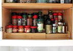 A neatly arranged shelf of spice jars in a kitchen cabinet