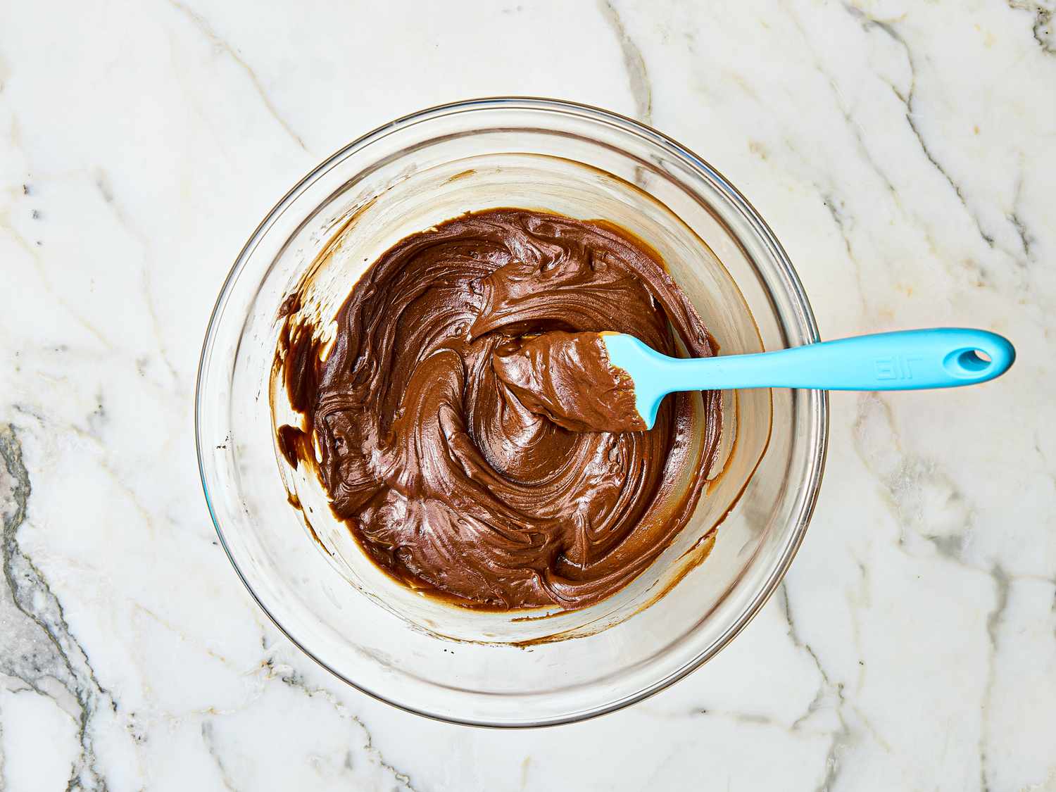 A bowl of chocolate mixture with a blue spatula on a marble surface
