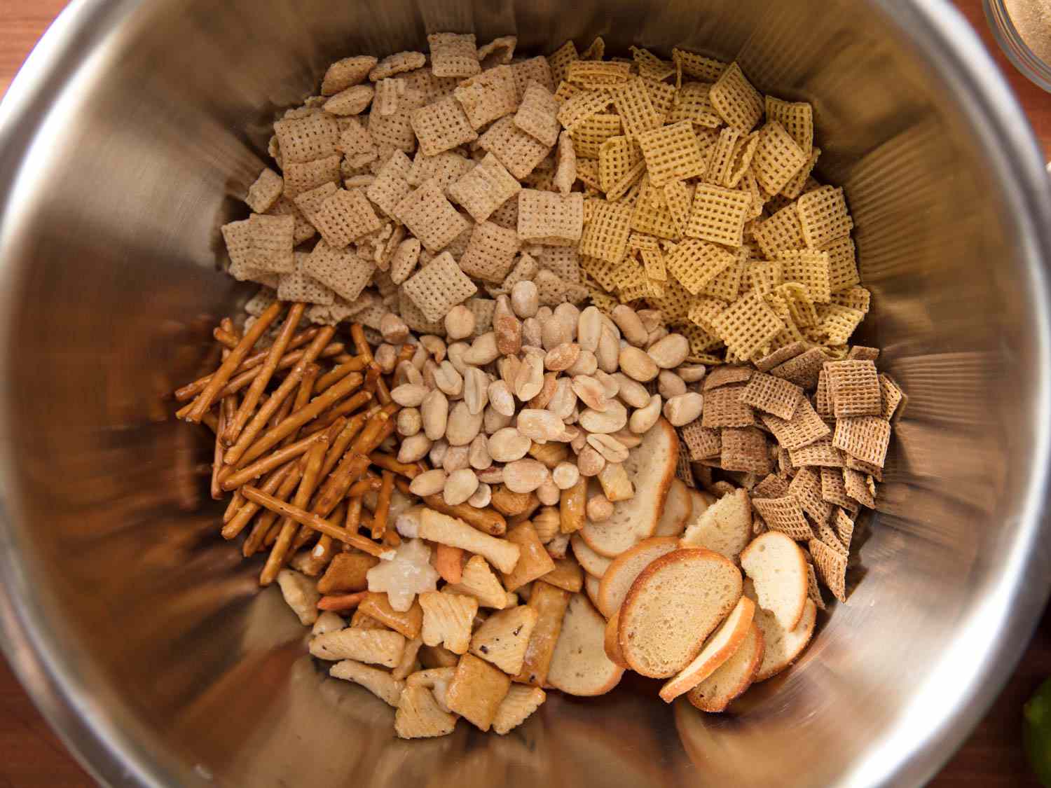 The chex mix components side-by-side in a metal mixing bowl.