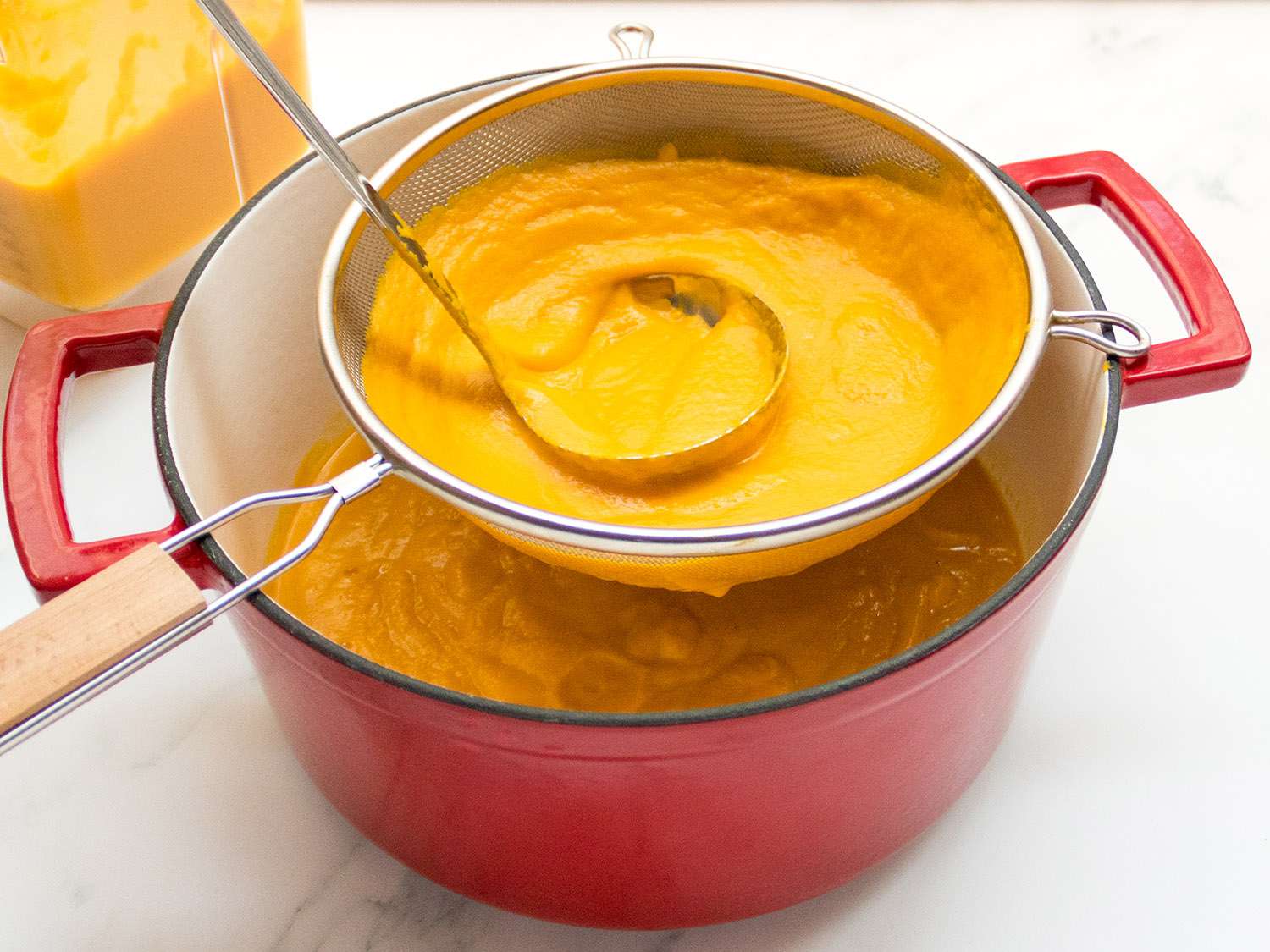 Carrot soup over a sieve.
