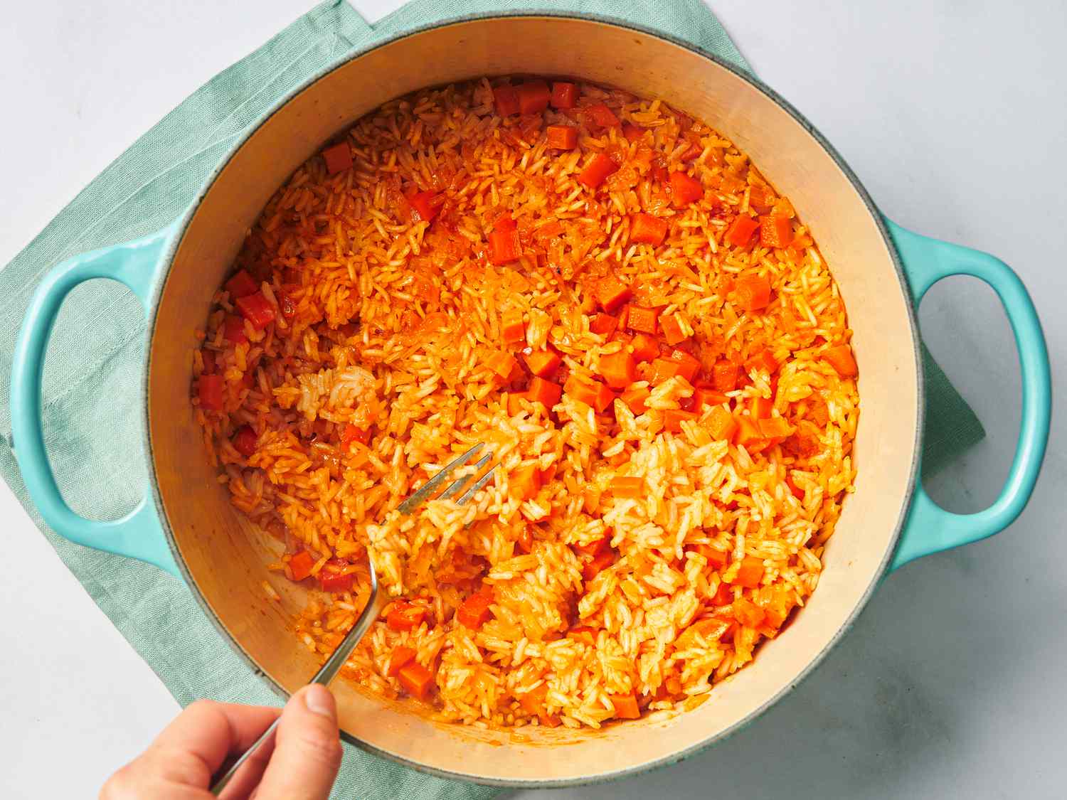 Cooked rice and the tomato and other vegetables, being fluffed in the Dutch oven with a fork.
