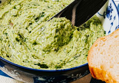 Butter being scooped from a bowl with a knife loaf of bread in the foreground