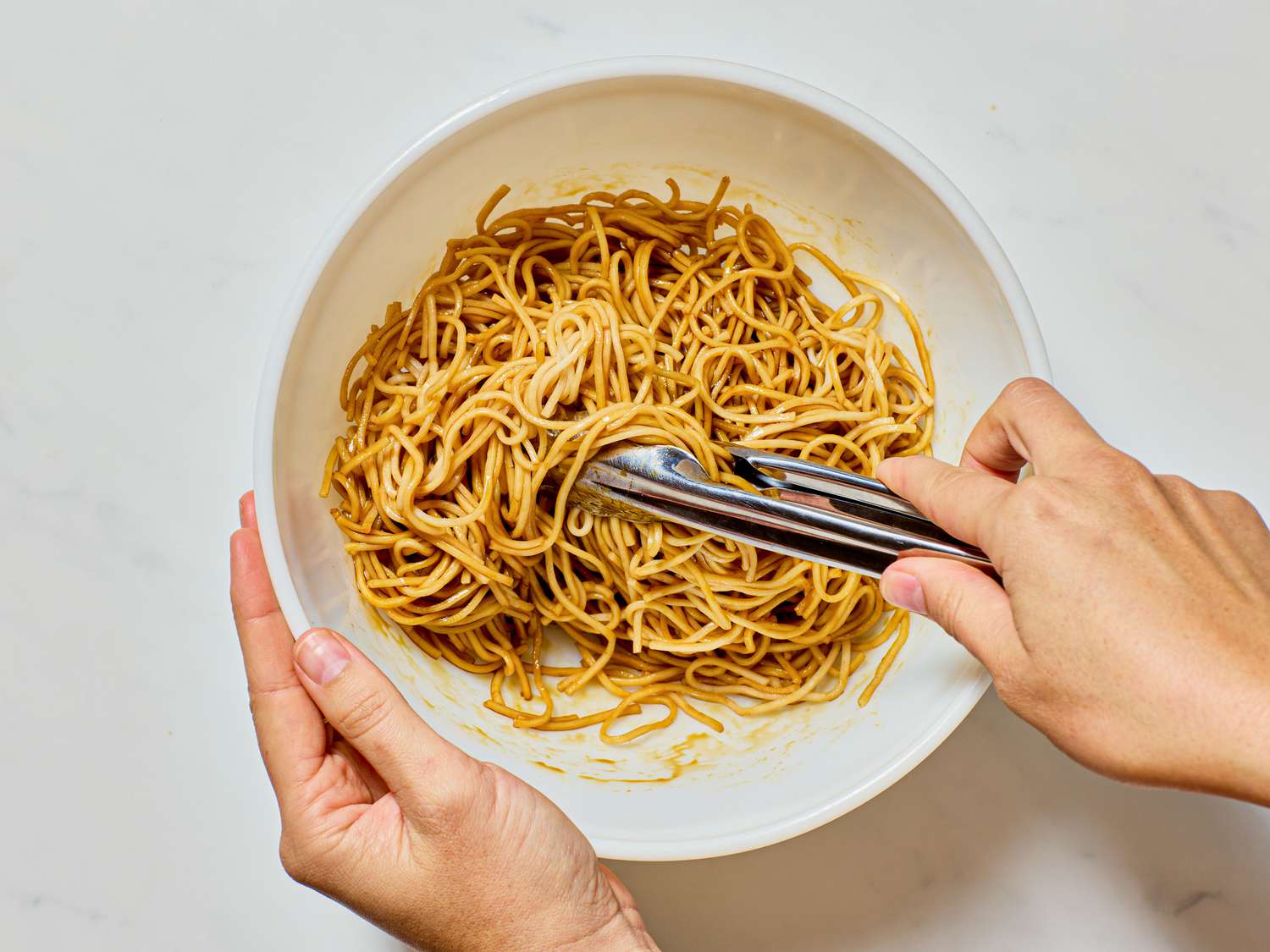 Tossing noodles in a bowl with tongs.