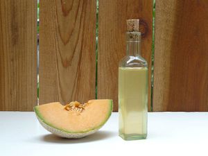 A bottle of homemade melon liqueur set on a table next to a large wedge of cantaloupe.