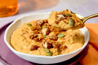 A bowl of pumpkin rice pudding garnished with nuts and seeds with a spoonful being lifted