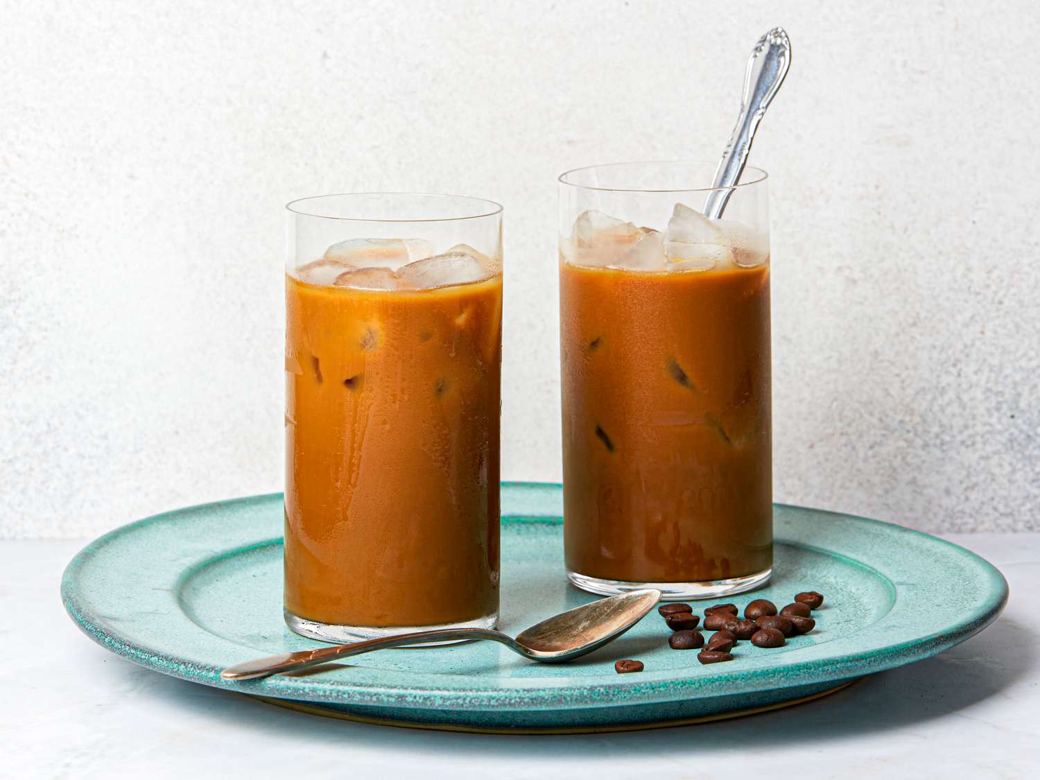 Two glasses of Vietnamese iced coffee on a blue plate with coffee beans.