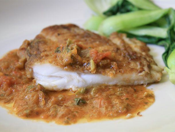 Skate wing served with tomato and caper sauce on a white plate. 