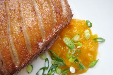 Closeup of a seared duck breast next to a puddle of apricot compote, sprinkled with sliced scallion.